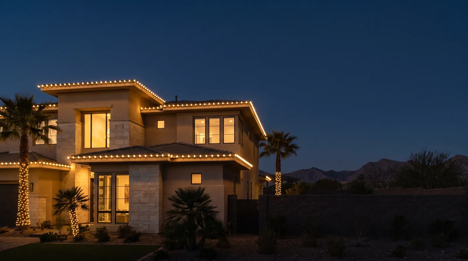 Two-story home at night with C9 bulbs along every roofline and wrapped palms, a quiet desert sky beside it